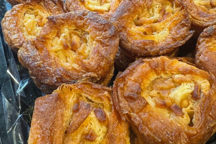 Rows of caramelized pastries with a flaky, golden-brown crust on a tray.