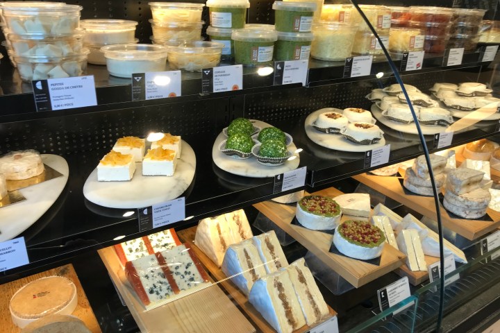 Display case with various cheeses, including round, sliced, and packaged types on shelves.