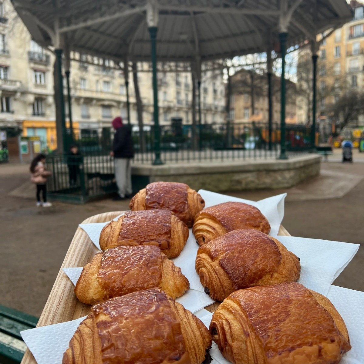 Tray of pastries in front of a park gazebo with people around.